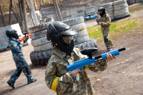 Teens dressed in camouflage playing paintball outdoors.