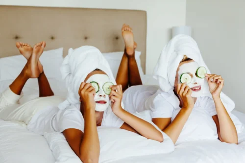 Two teenage girls relaxing with face masks and cucumber slices on a spa day.